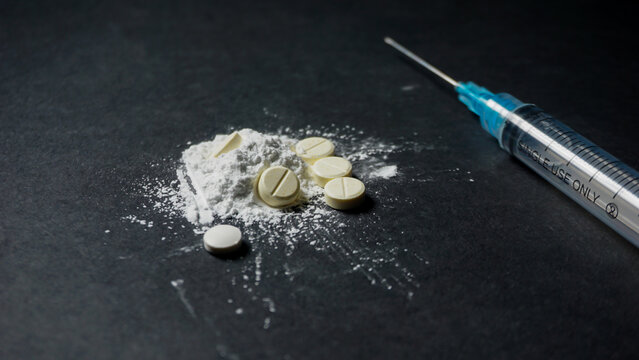 syringe and pills. Disposable medical syringe with some illegal white drugs in powder and pill form. Misused drugs concept. 