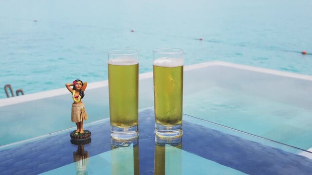 Beer. Glass of beer by hotel pool and hula dancer doll. Luxury resort travel vacation concept. Raw real unedited video.
