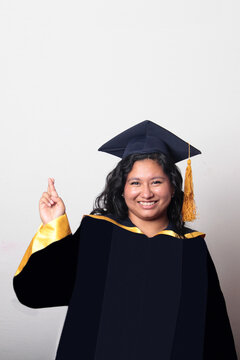 Young, dark-haired Latina woman dressed in a cap and gown is happy and excited to celebrate her graduation