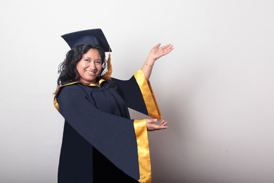 Young, dark-haired Latina woman dressed in a cap and gown is happy and excited to celebrate her graduation