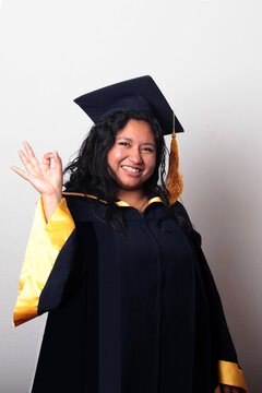 Young, dark-haired Latina woman dressed in a cap and gown is happy and excited to celebrate her graduation