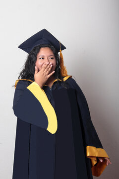 Young, dark-haired Latina woman dressed in a cap and gown is happy and excited to celebrate her graduation