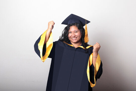 Young, dark-haired Latina woman dressed in a cap and gown is happy and excited to celebrate her graduation