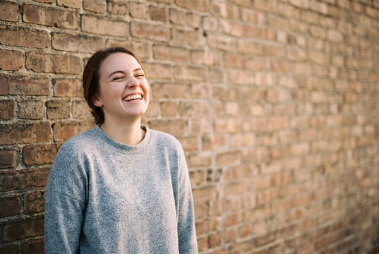 Woman laughing against urban brick wall outdoors portrait