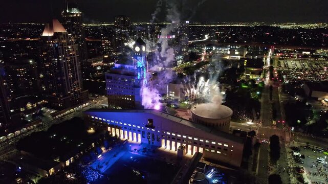 Aerial view of colorful fireworks exploding over historic city hall at night.