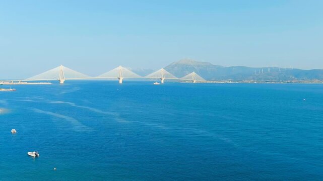 Patras, Greece. The Rio-Antirrio Bridge, a multi-span cable-stayed structure with four white pylons spanning the Gulf of Corinth, Drone footage under clear blue sky. Drone footage