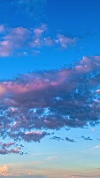 Clouds drift across a vibrant blue sky at sunset in a vertical timelapse view