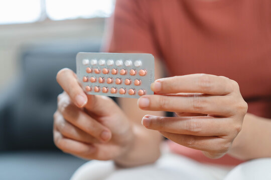 Close up woman holding oral contraceptive birth control pills blister pack and a glass of water, concept of unwanted pregnancy prevention and female healthcare.