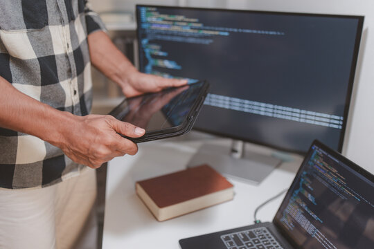 Software developer coding on laptop and tablet in a modern workspace. Close-up of programming workflow, software engineering, debugging source code, and multi-device application development.