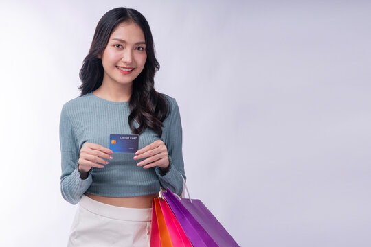Happy young Asian woman holding a credit card and colorful shopping bags, smiling beautifully at camera. Isolated on white background. Perfect for banking, e-commerce and retail concepts.