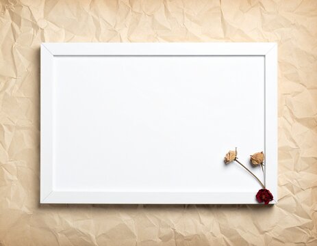 Empty white picture frame with dried flowers on a crumpled paper background.