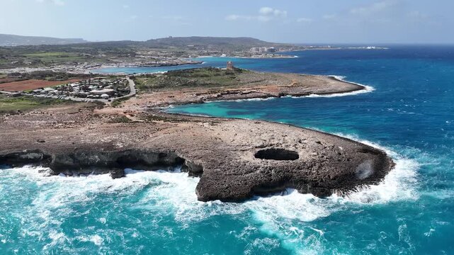 coastal watchtower overlooks coral lagoon headland malta turquoise cove waves crash rocky shoreline distant hilltop town sprawls green fields aerial panorama mediterranean coastline scenic