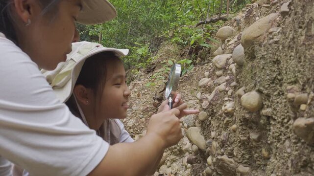 Asian mother and daughter looking through magnifying glass at geological rock stratum