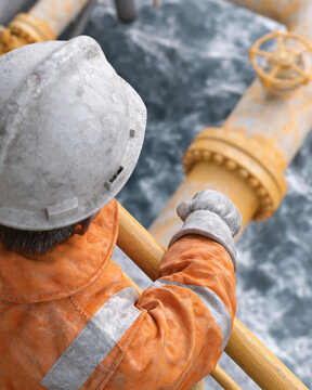 Worker grips pipeline railing. Hard hat shields head from elements. Orange jacket with reflective stripes. Hand rests firmly on metal structure. Ocean waves crash nearby