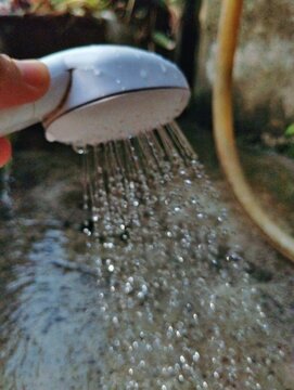 A showerhead with water spraying from it, captured in mid-air as individual droplets.