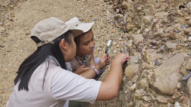 Asian mother and daughter looking through magnifying glass at geological rock stratum