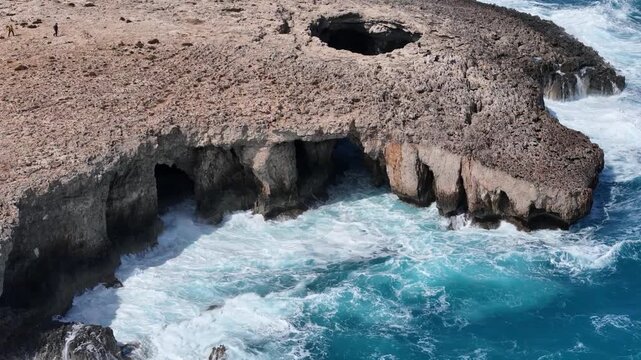 blowhole coral lagoon headland malta sea caves honeycomb weathered rock undercut cliff base hikers stand near rim turquoise water surges below aerial view natural sinkhole erosion formation coastline
