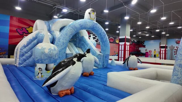 Indoor children inflatable playground with arctic penguin theme and slides.