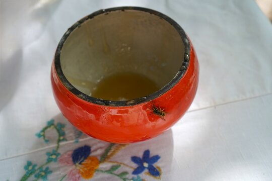 Fresh liquid honey in a ceramic pot with a wasp on a vintage embroidered linen tablecloth. Traditional Slavic Honey Spas holiday concept, authentic rustic still life, and natural sweetness