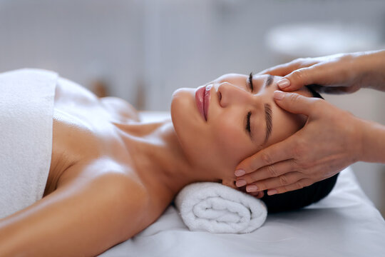 Young woman relaxing with closed eyes while enjoying soothing facial and scalp massage during luxurious spa wellness treatment, closeup