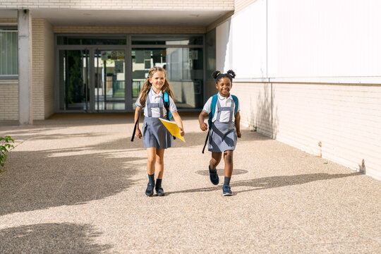 Happy multiethnic girls wearing school uniforms and backpacks, walking together to class on the first day of school