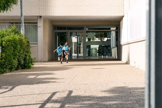 Excited diverse schoolgirls with backpacks hurrying towards the school entrance, embracing friendship and the start of a new academic year