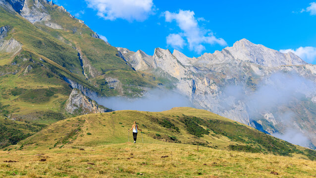 Woman hiker walking on a green ridge towards misty rocky peaks in the alps- Freedom, Adventure, active lifestyle