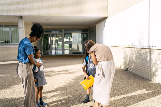 Multiethnic mothers standing with their daughters in school uniforms, preparing them for the first day of school