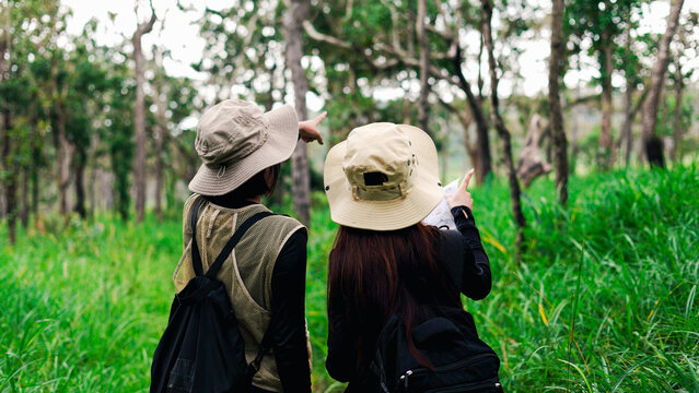 Two female hikers with backpacks pointing at scenery while exploring a lush green forest trail.