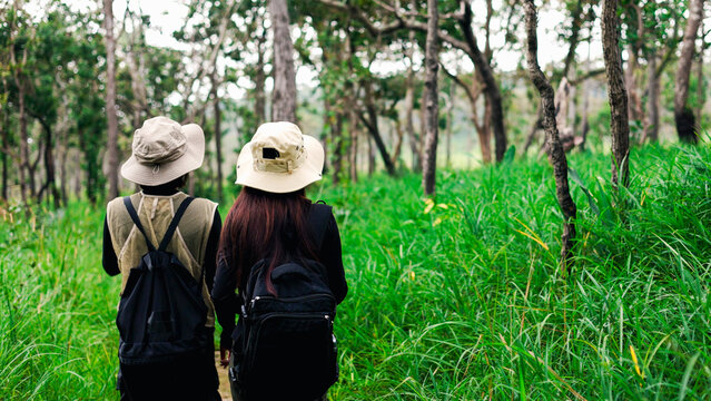 Two female hikers with backpacks pointing at scenery while exploring a lush green forest trail.