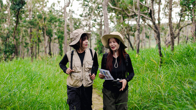 Two female hikers with backpacks pointing at scenery while exploring a lush green forest trail.