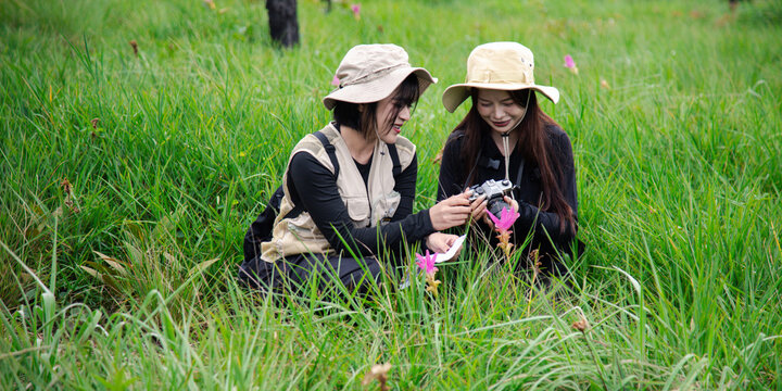 Two happy young Asian female friends hiking together in green forest, carrying backpacks, enjoying eco travel and nature.