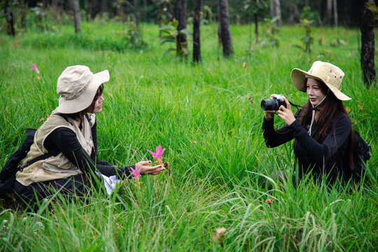 Two happy young Asian female friends hiking together in green forest, carrying backpacks, enjoying eco travel and nature.