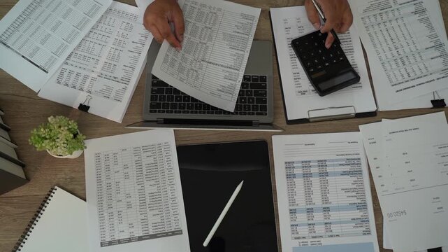 Accountant reviewing financial reports over laptop with calculator, tablet, printed documents for accounting, tax preparation, audit, bookkeeping, financial planning.