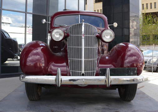 Ufa, republic of Bashkortostan, Russia- 04.26.2026. Front view of a dark red classic vintage Oldsmobile car with chrome details. Urban outdoor photography with reflections. 