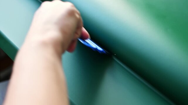 Hand smooths adhesive vinyl film onto green kitchen cabinet facade with plastic squeegee during furniture surface renovation