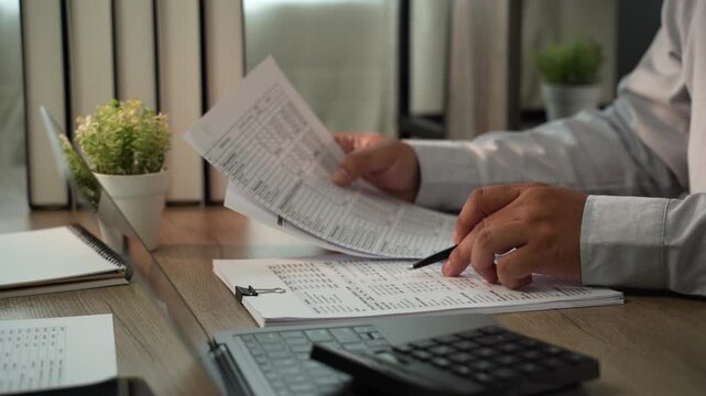 Accountant pointing at financial report with pen beside laptop and calculator for accounting, tax preparation, audit, bookkeeping, financial planning.