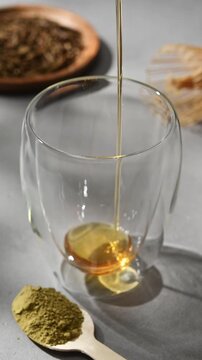 Golden syrup pours into clear double wall glass beside hojicha powder, creating sweet base for homemade roasted tea drink.
