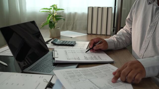 Accountant pressing calculator with pen on financial documents for tax preparation, accounting, audit, bookkeeping, financial planning in office.