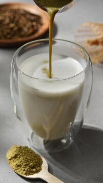 Concentrated hojicha tea is poured into foamed milk in glass, creating creamy roasted Japanese tea latte in vertical closeup.