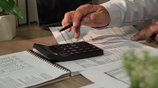 Close up accountant hand using calculator on financial reports during tax season for accounting, tax preparation, audit, bookkeeping, financial planning.