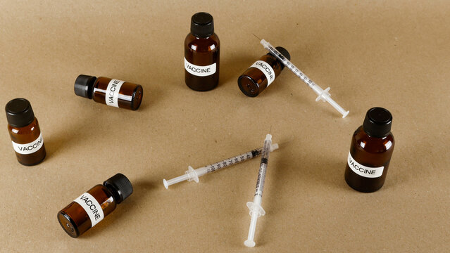 Vaccine vials and medical syringes scattering across a plain brown background, representing immunization campaigns, disease prevention, and healthcare solutions