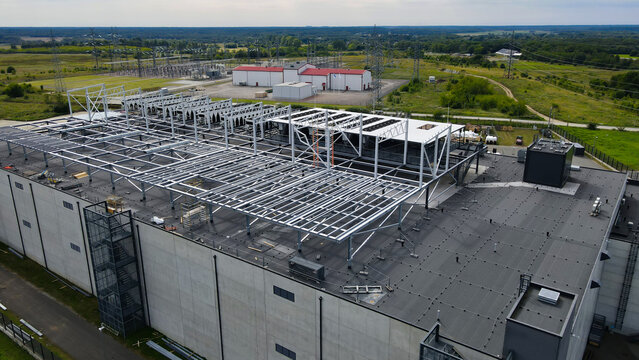 Data center building under construction, featuring extensive rooftop steel framework for future cooling systems and an adjacent electrical substation providing critical power infrastructure