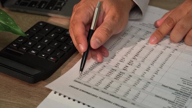 Accountant calculating figures on financial reports with pen for financial planning, accounting, bookkeeping, tax preparation, budget review.