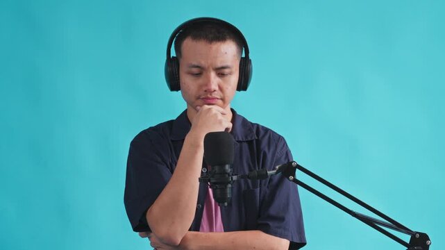 Thoughtful podcast host wearing headphones touching chin while contemplating ideas near studio microphone

