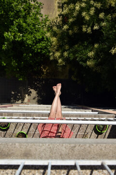 Young woman in floral dress sitting on the edge of a terrace in an apartment building, playful urban summer vibe downward view