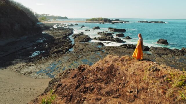 Woman in yellow dress walking on rocky coast by ocean in sunny Costa Rica