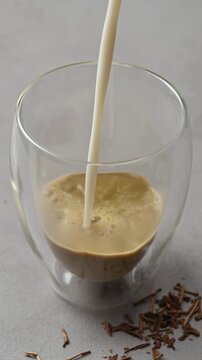 Oat milk pours into hojicha in double wall glass, mixes with roasted tea and creates creamy foam during latte preparation.