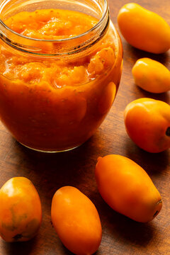 Tomato puree made from unique Orange Banana heritage tomatoes, packed in a glass barrel jar, set against a wooden background surrounded by fresh, whole Orange Banana tomatoes ; moody food photography.