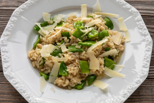Macro close-up of creamy Italian risotto with green sugar snap pea pieces and parmesan flakes filling the white plate and frame
